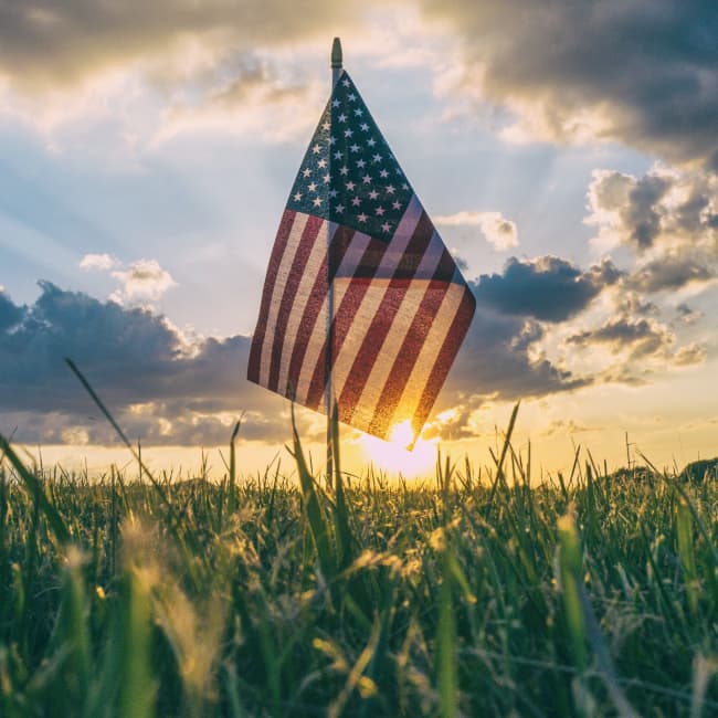 An American flag in the middle of a field at sunset